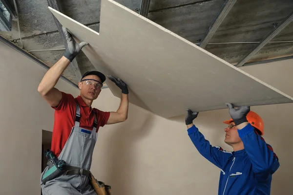 Imagem de dois homens instalando no teto forros de drywall.