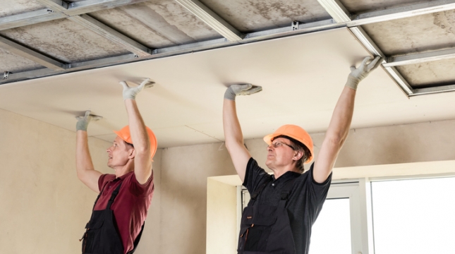 Dois homens intalando placa de drywall no teto.